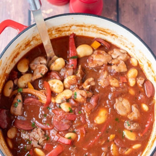 Overhead view of one pot spanish chicken and chorizo stew in a large casserole pot with a serving spoon in. Salt and pepper cellars at the top.