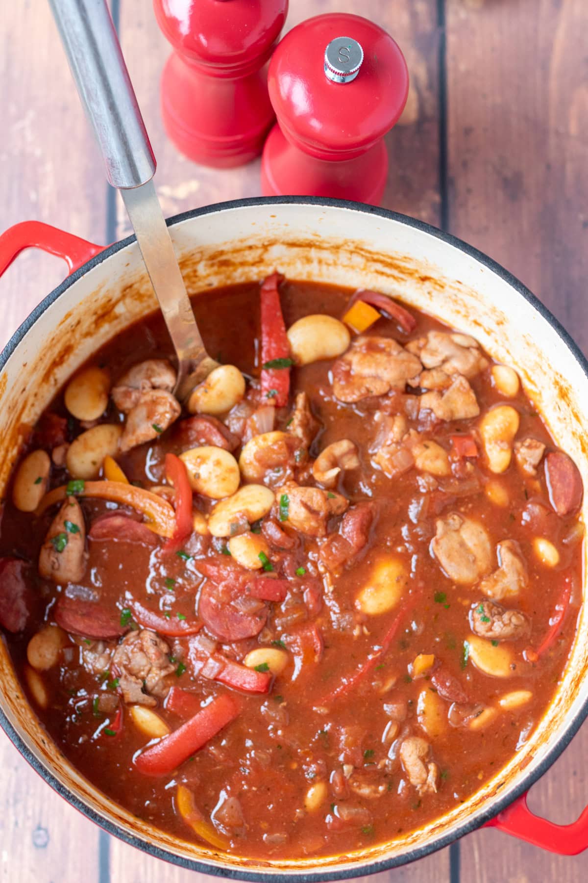 Overhead view of one pot spanish chicken and chorizo stew in a large casserole pot with a serving spoon in. Salt and pepper cellars at the top.
