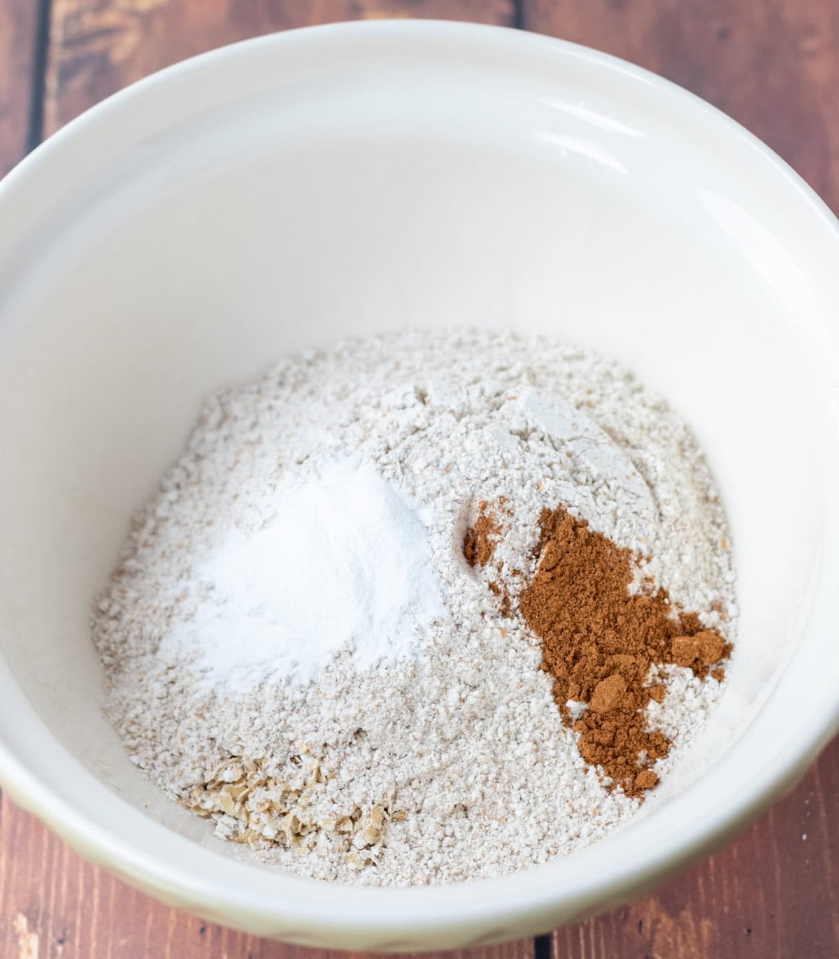A large bowl with oats, flour, baking powder, and cinnamon in.