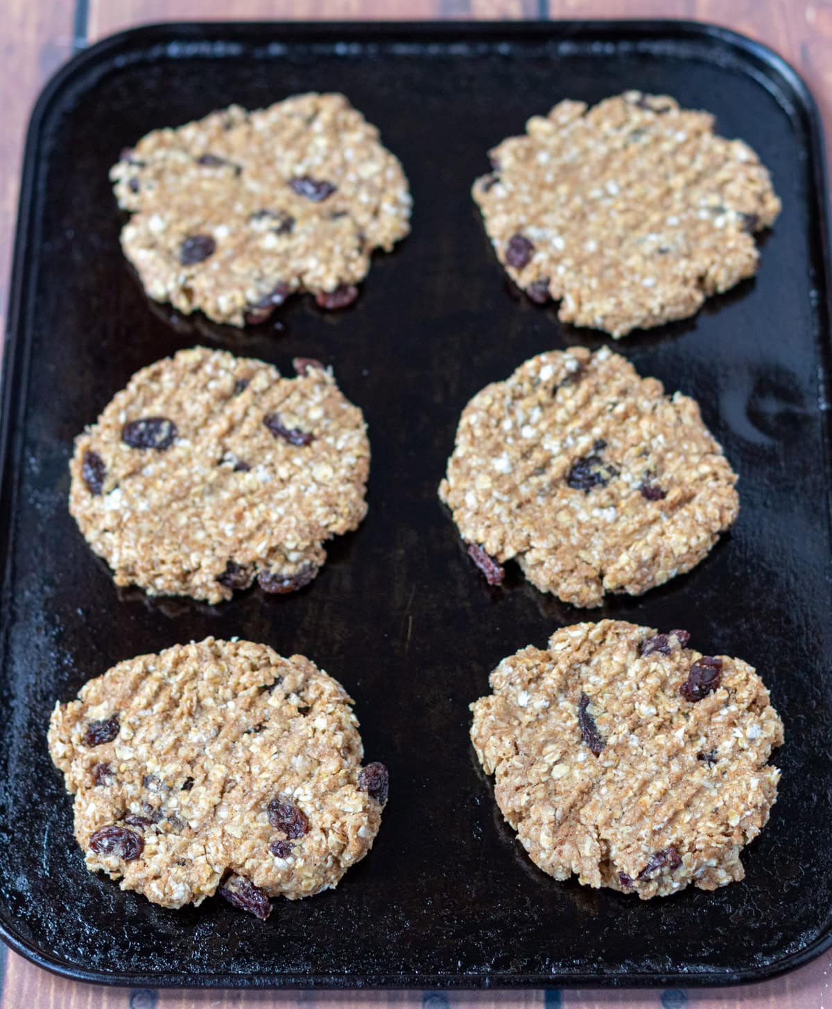 Six rolled out raisin oat cookied on a baking tray ready to go into the oven.