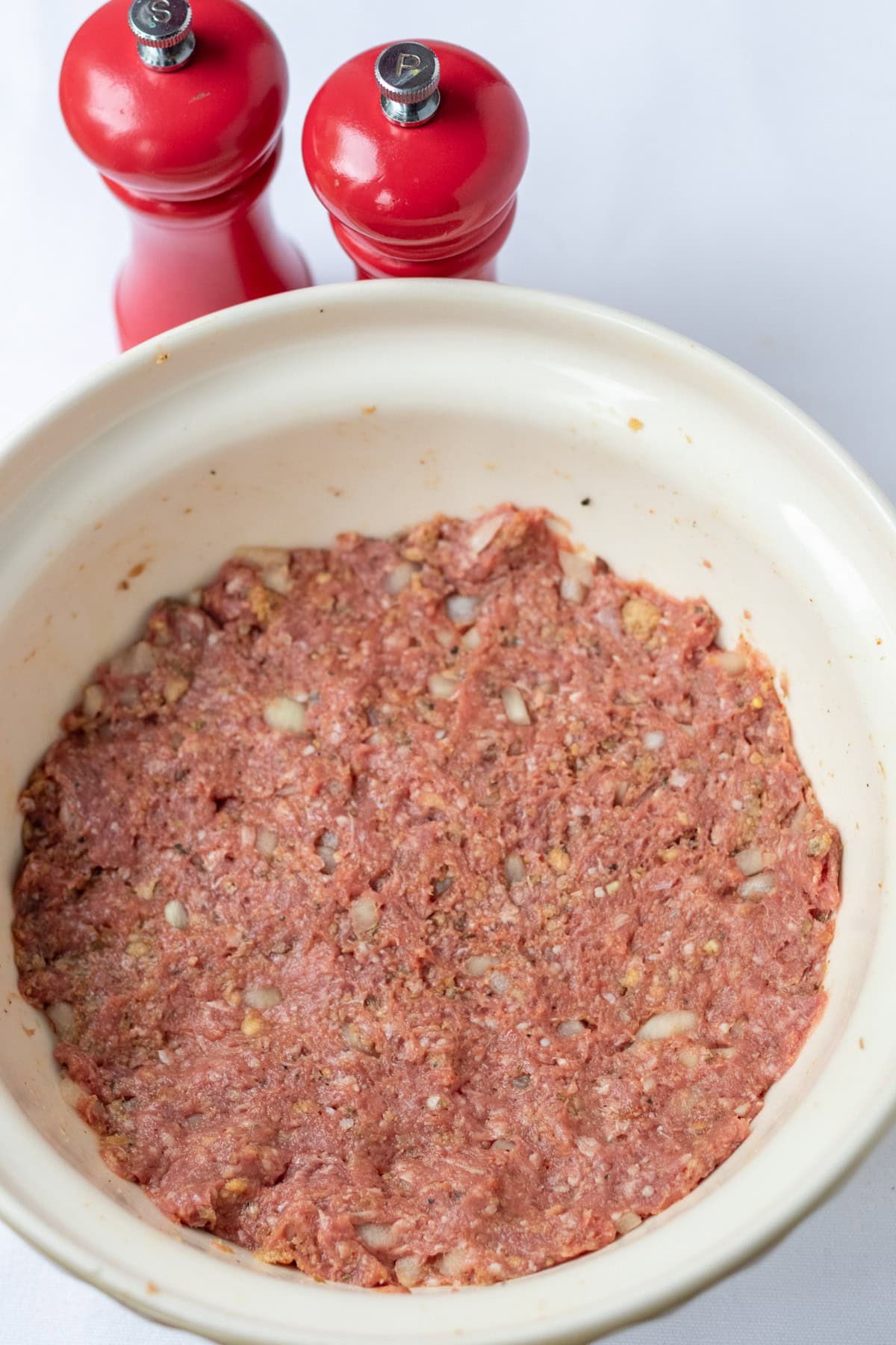 Lamb burger ingredients in a large mixing bowl well mixed. Salt and pepper cellars above.