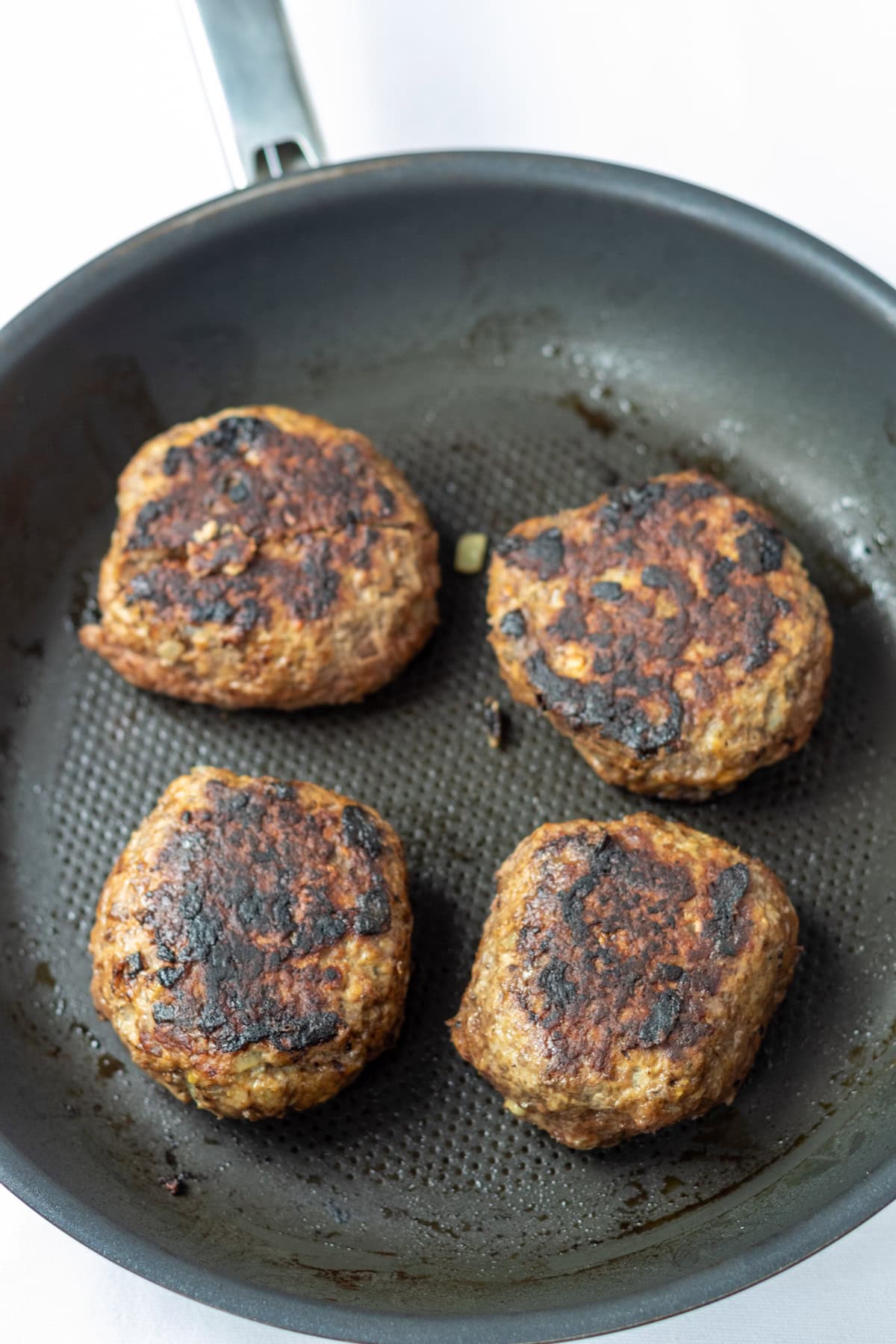 4 cooked lamb burgers in a non-stick pan.