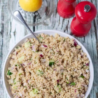 Overhead view of a serving dish of quick tuna quinoa salad with a serving spoon in. Above half a lemon in a lemon juicer and salt and pepper cellars.