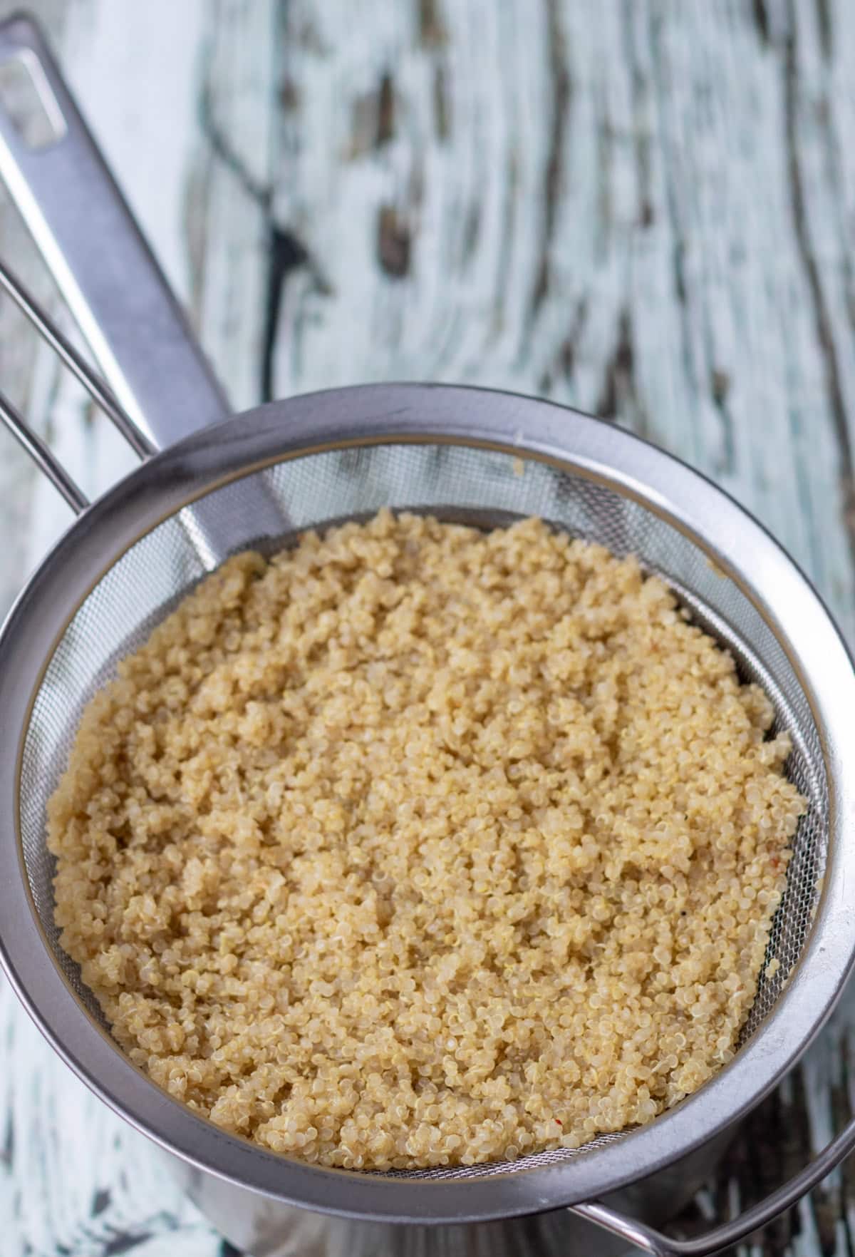 Cooked, drained quinoa in a sieve over a saucepan.