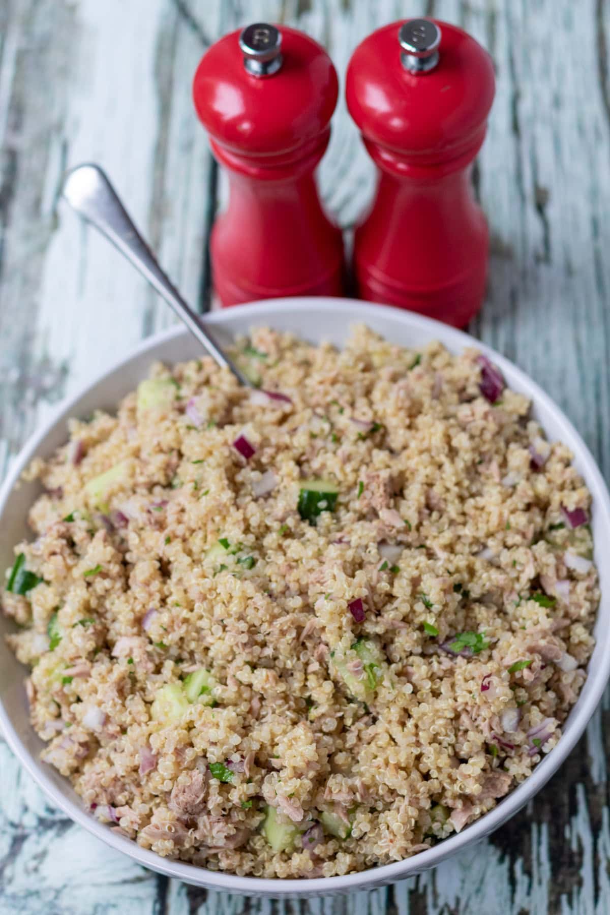 Quick tuna quinoa salad seasoned and served in a serving dish with a serving spoon in. Salt and pepper cellars behind.