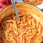 One pot turkey mince pasta in a large casserole pot with a serving spoon in. Behind is a portion served in a pasta bowl with salt and pepper cellars alongside.
