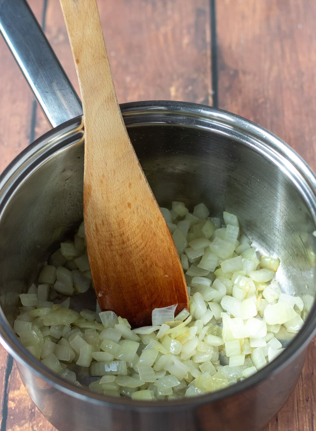 Chopped onion cooked in a large saucepan with a wooden spoon in.