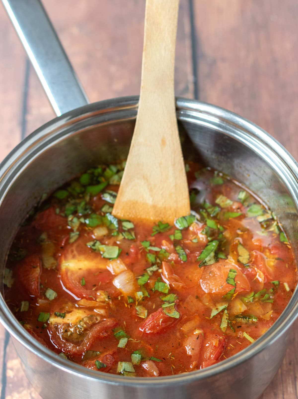 Roasted tomatoes, garlic, stock, basil and chopped tomatoes all being stirred in a large saucepan.